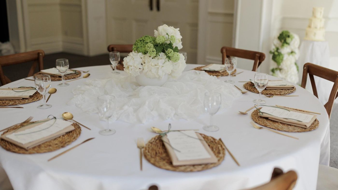A round table laid with white linen and gold chargers