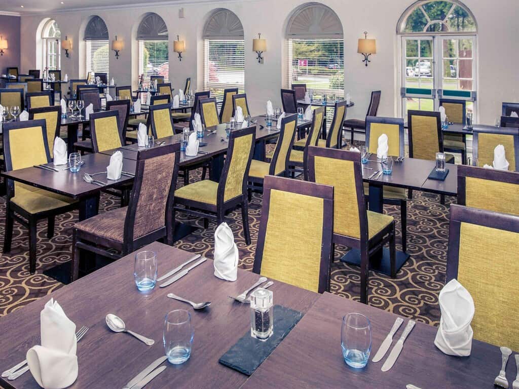 Spacious hotel restaurant with stylish decor, large windows, and prepared tables for a dining experience.