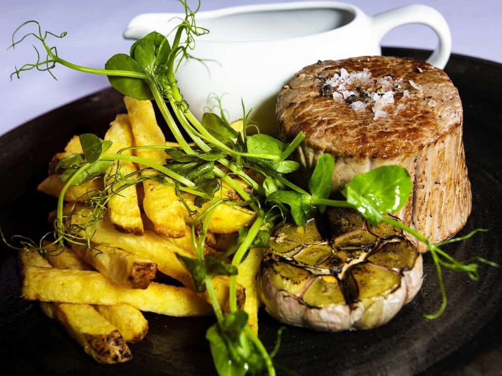 A delicious plate featuring perfectly cooked steak, crispy French fries, sautéed mushrooms, and fresh greens, perfect for a fine dining experience.