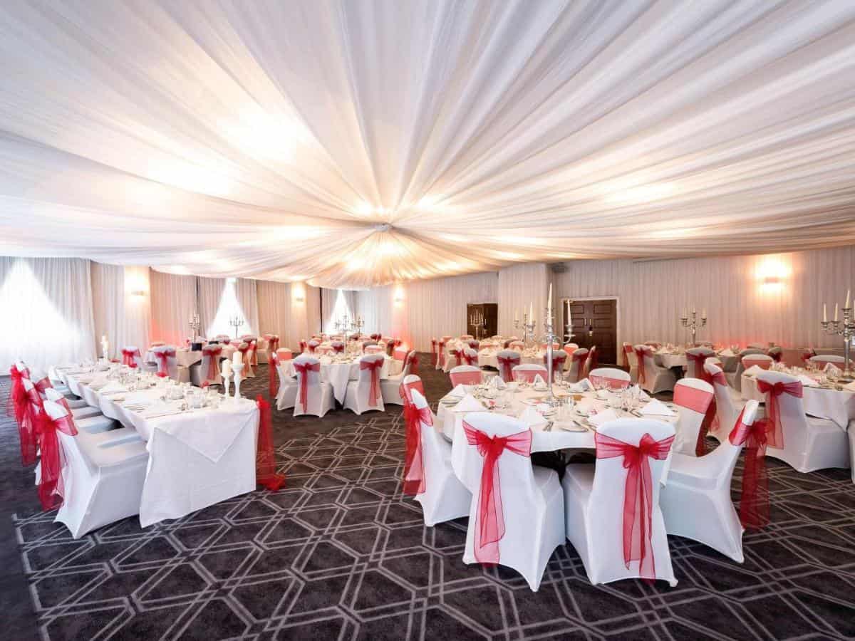 Stylish banquet hall decorated for special events with white linens, red accents, and candlelit centerpieces.