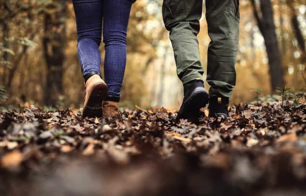 Close-up of people walking in fallen leaves in an autumn forest setting, highlighting outdoor adventure and nature.
